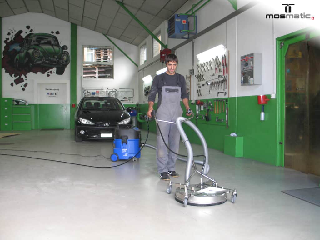 Mitarbeiter reinigt den Werkstattboden mit einem fahrbaren Flächenreiniger.