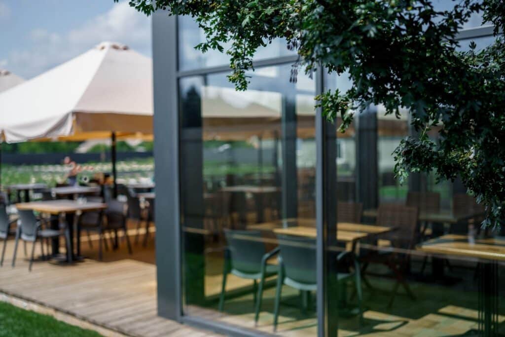Bestuhlte Außenterrasse eines Restaurants mit Holzboden, Sonnenschirm und Glasfassade